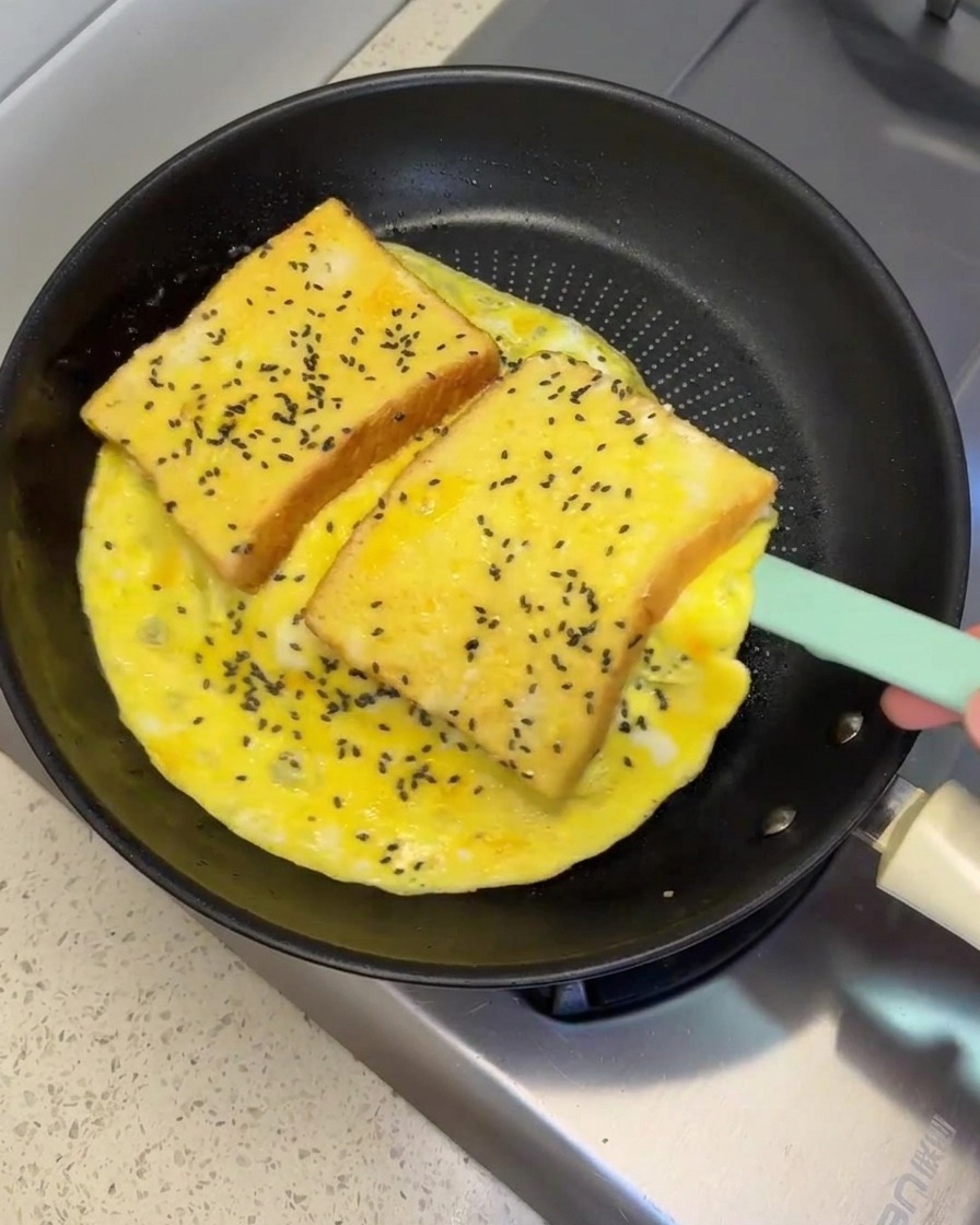 Silikonowa łopatka unosząca i obracająca duży omlet jajeczny z dwiema kromkami chleba.