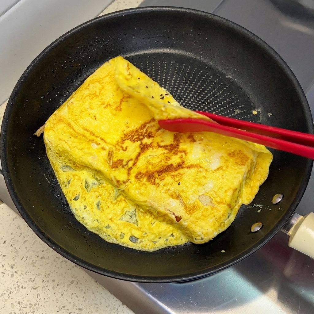 Czerwone silikonowe szczypce zaganiające wystające brzegi omletu na kromki chleba.
