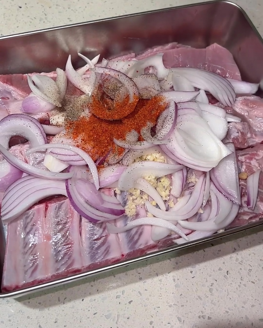 Kopczyk czerwonego chili, czarnego pieprzu i brązowego cukru na surowych żeberkach i czerwonej cebuli w metalowej tacy.