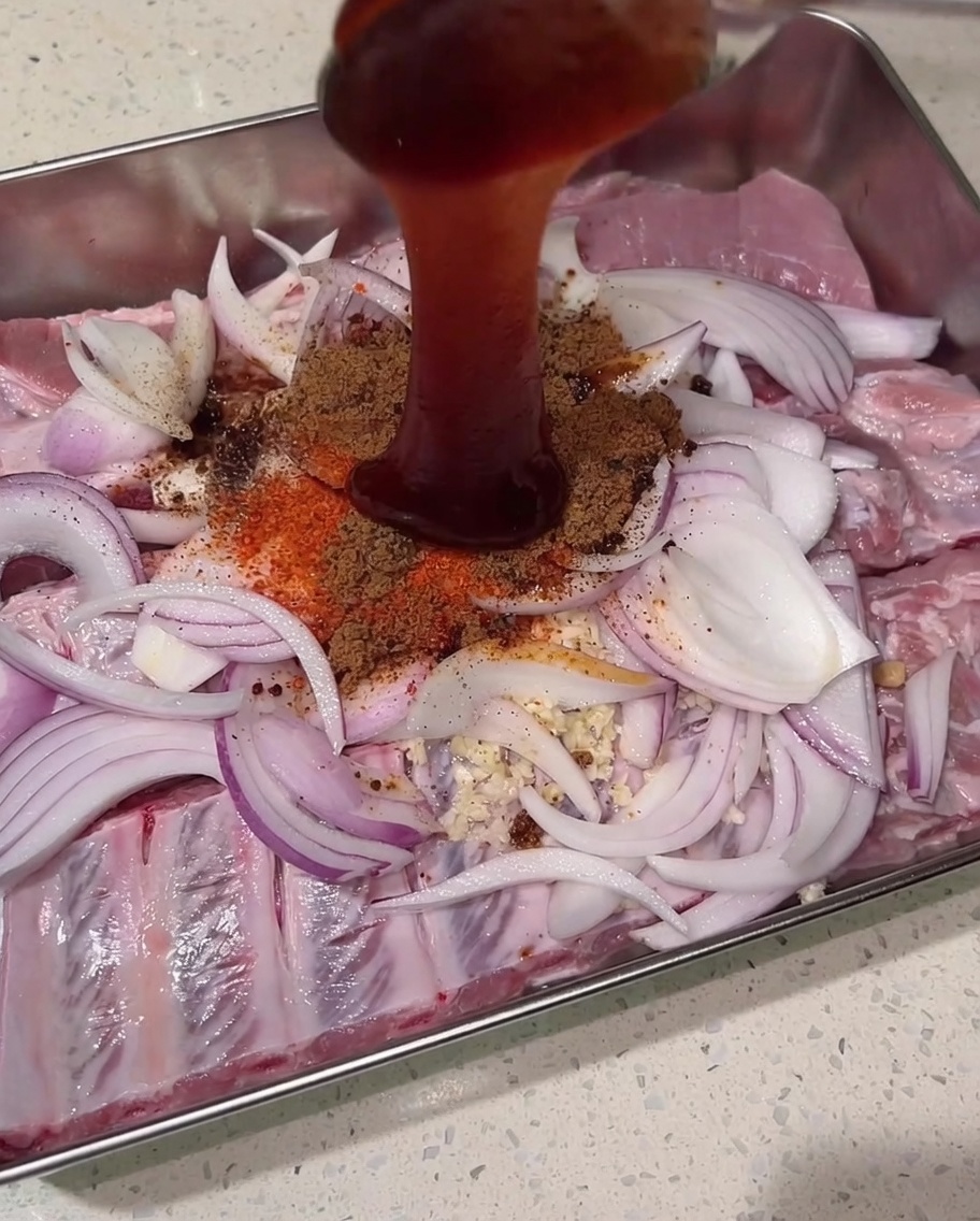Gęsty, ciemnoczerwony sos char siu lany z góry na suche przyprawy, surowe żeberka i cebulę.