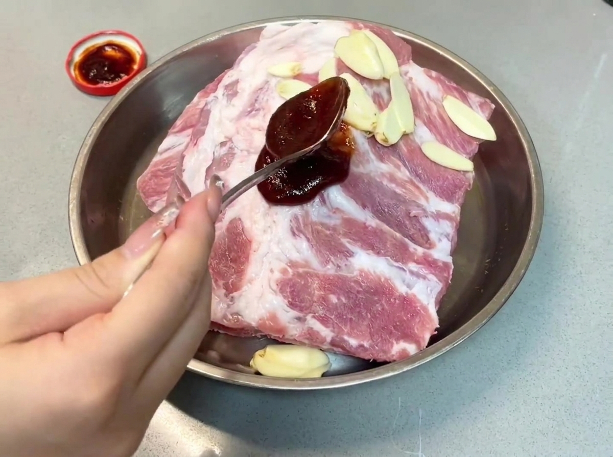 Łyżka ciemnego sosu char siu wylewana na żeberka wieprzowe w metalowej tacy.