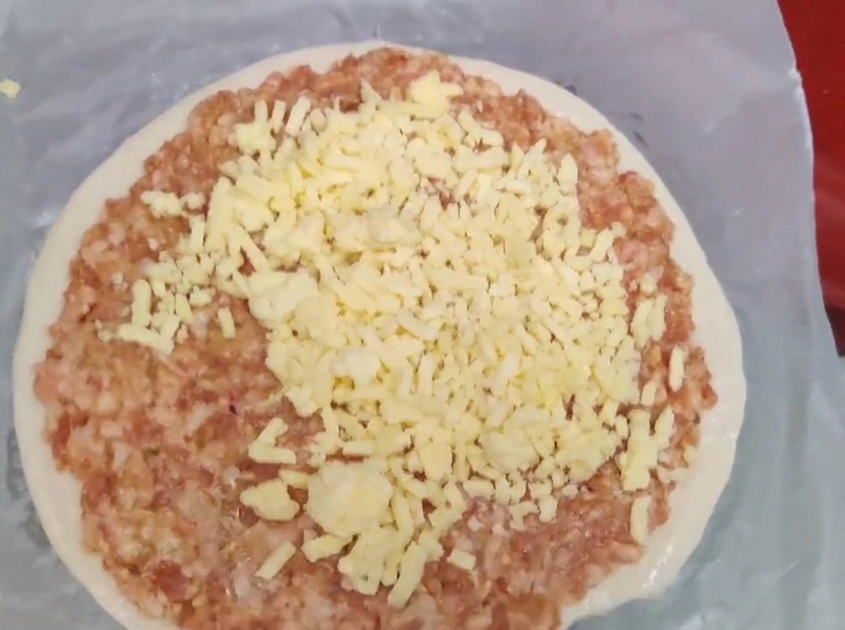 Starty żółty ser ułożony na warstwie surowego mielonego mięsa na placku z cebulką.