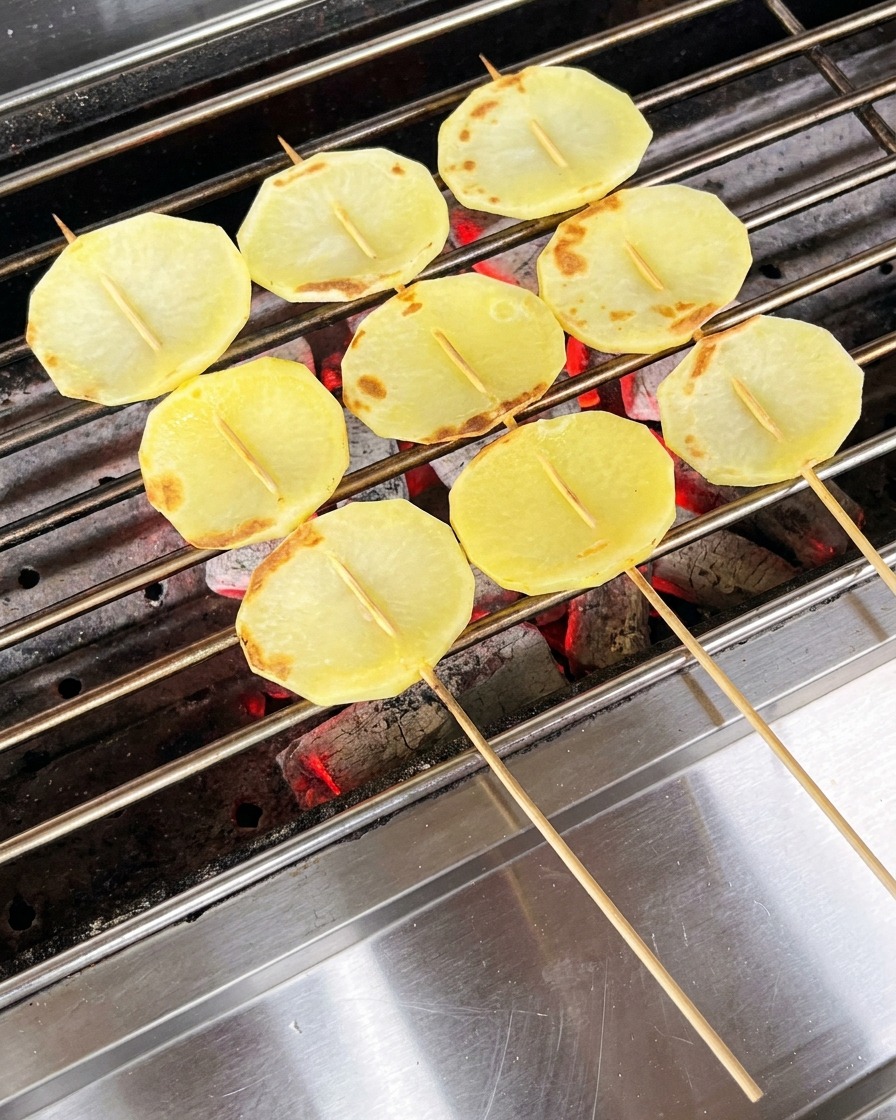 Częściowo ugotowane plasterki ziemniaków na grillu smarowane olejem za pomocą pędzla.