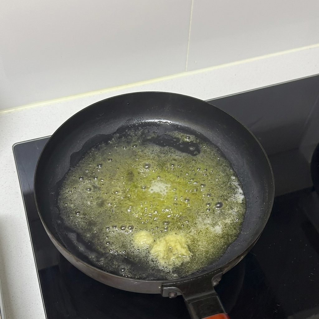 Posiekany czosnek gotujący się w roztopionym maśle na patelni.