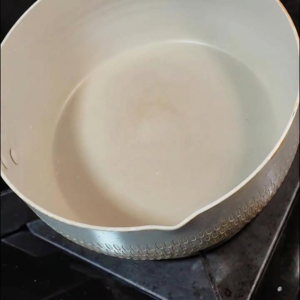 Kawałek masła rozpuszczający się na białej ceramicznej patelni na kuchence.