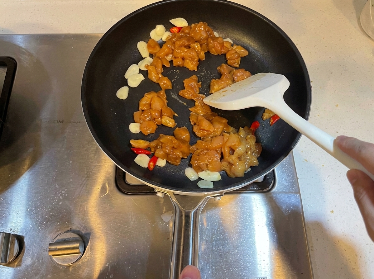 Zamarynowane kawałki kurczaka w kostce smażone na patelni z czosnkiem i chili.