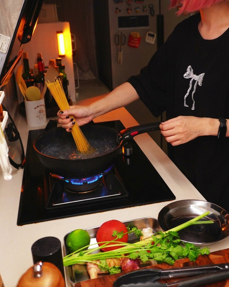 Suchy makaron spaghetti zanurzany w garnku z gotującą się wodą na kuchence.
