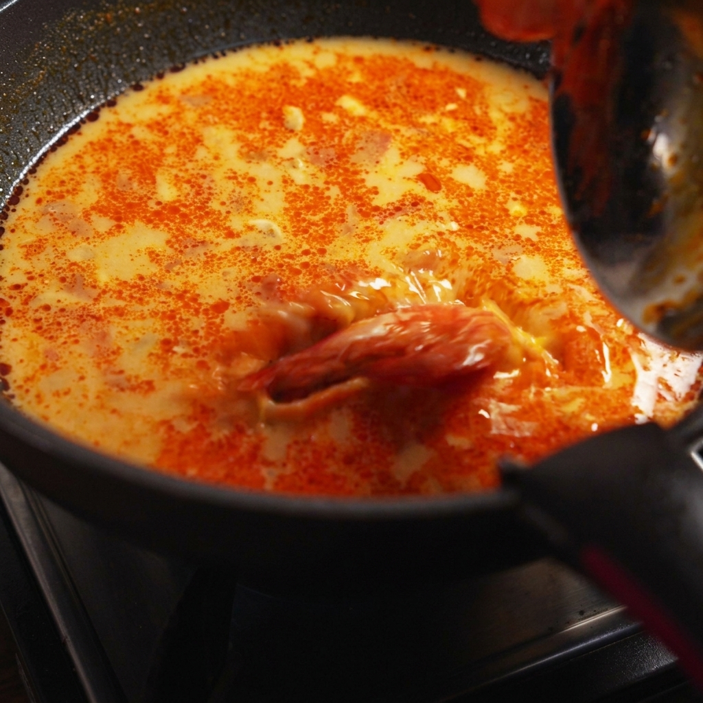 Ugotowany makaron spaghetti, krewetki i świeża kolendra wrzucane na patelnię z gotującym się sosem.
