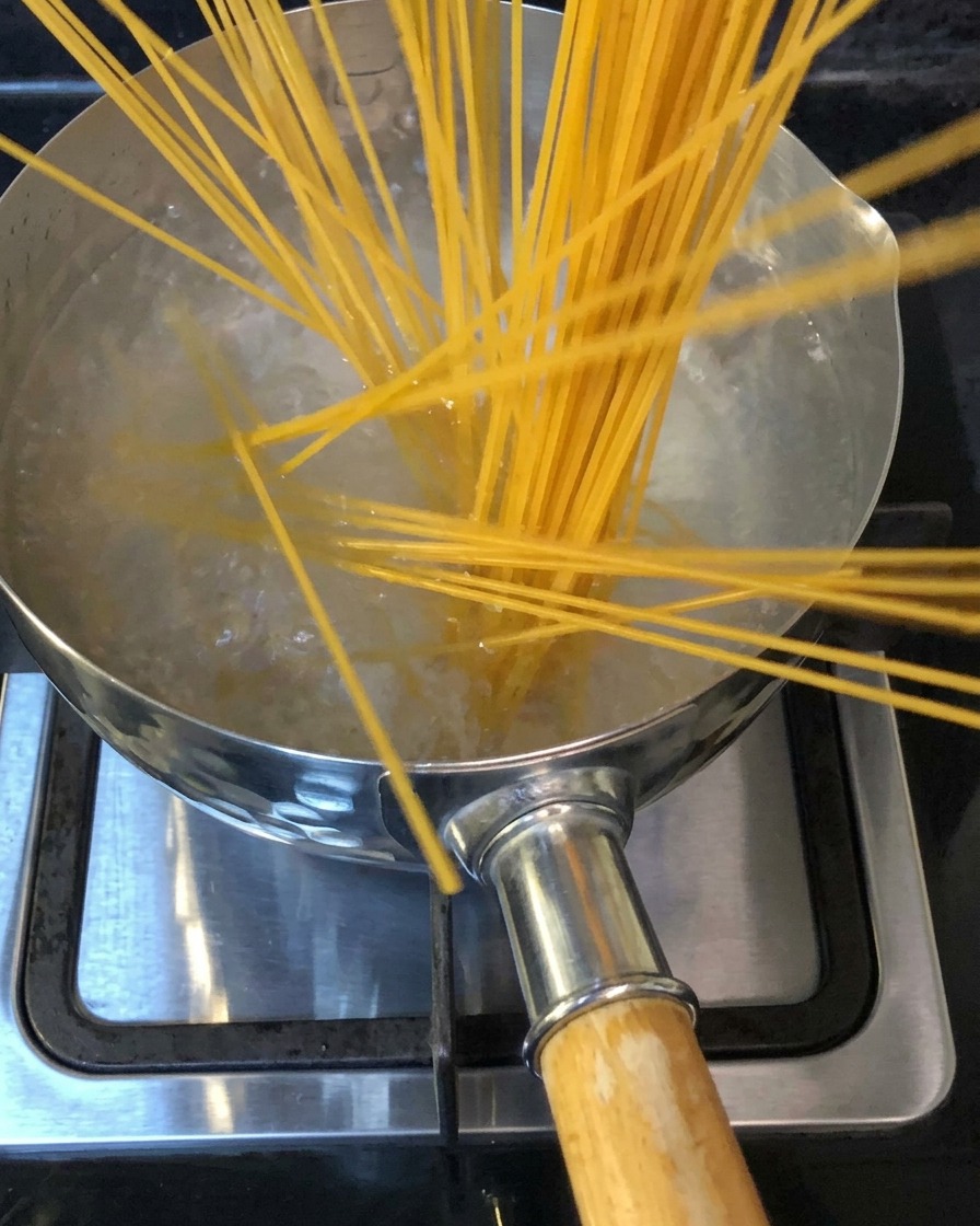 Nietoperze makaronu spaghetti zanurzano w garnku z wrzącą osoloną wodą na kuchence.