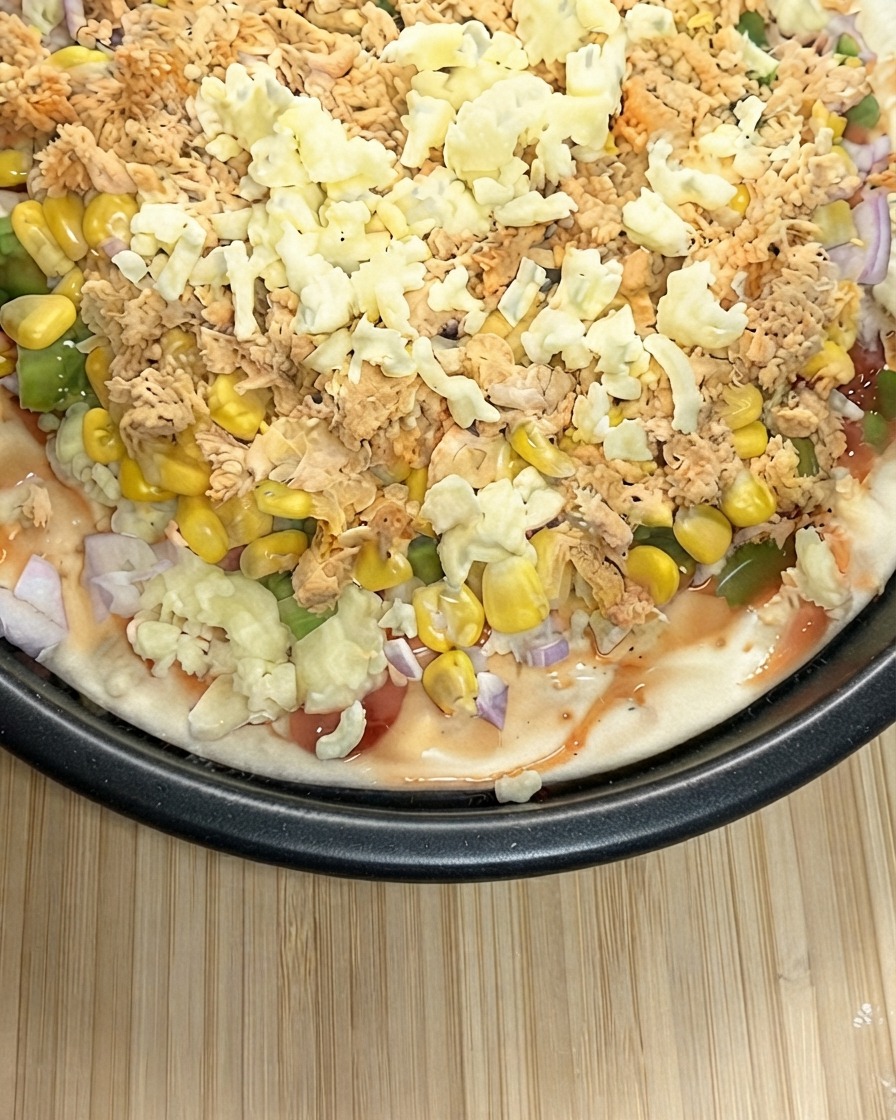 Zbliżenie przygotowywanej pizzy obficie posypanej grubą warstwą startego sera mozarella.