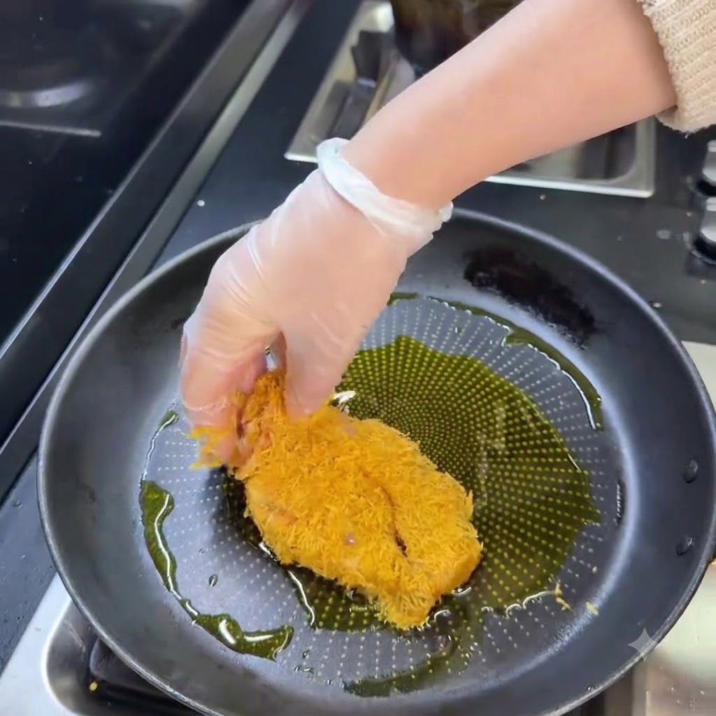 Panierowany kotlet schabowy smażący się na patelni z gorącym olejem na złoty kolor.