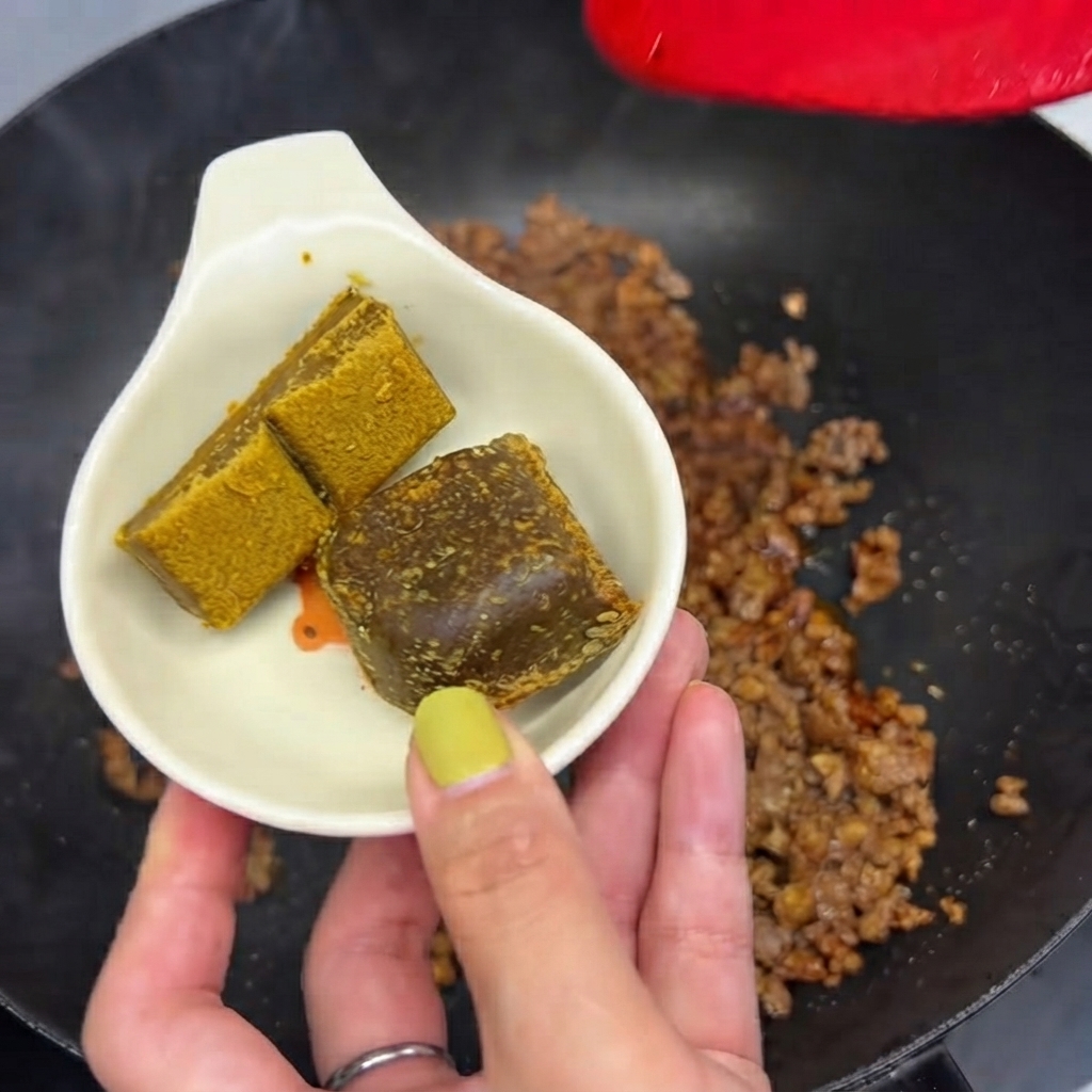 Dwie kostki curry w małym białym naczyniu, gotowe do wrzucenia na patelnię z mielonym mięsem.