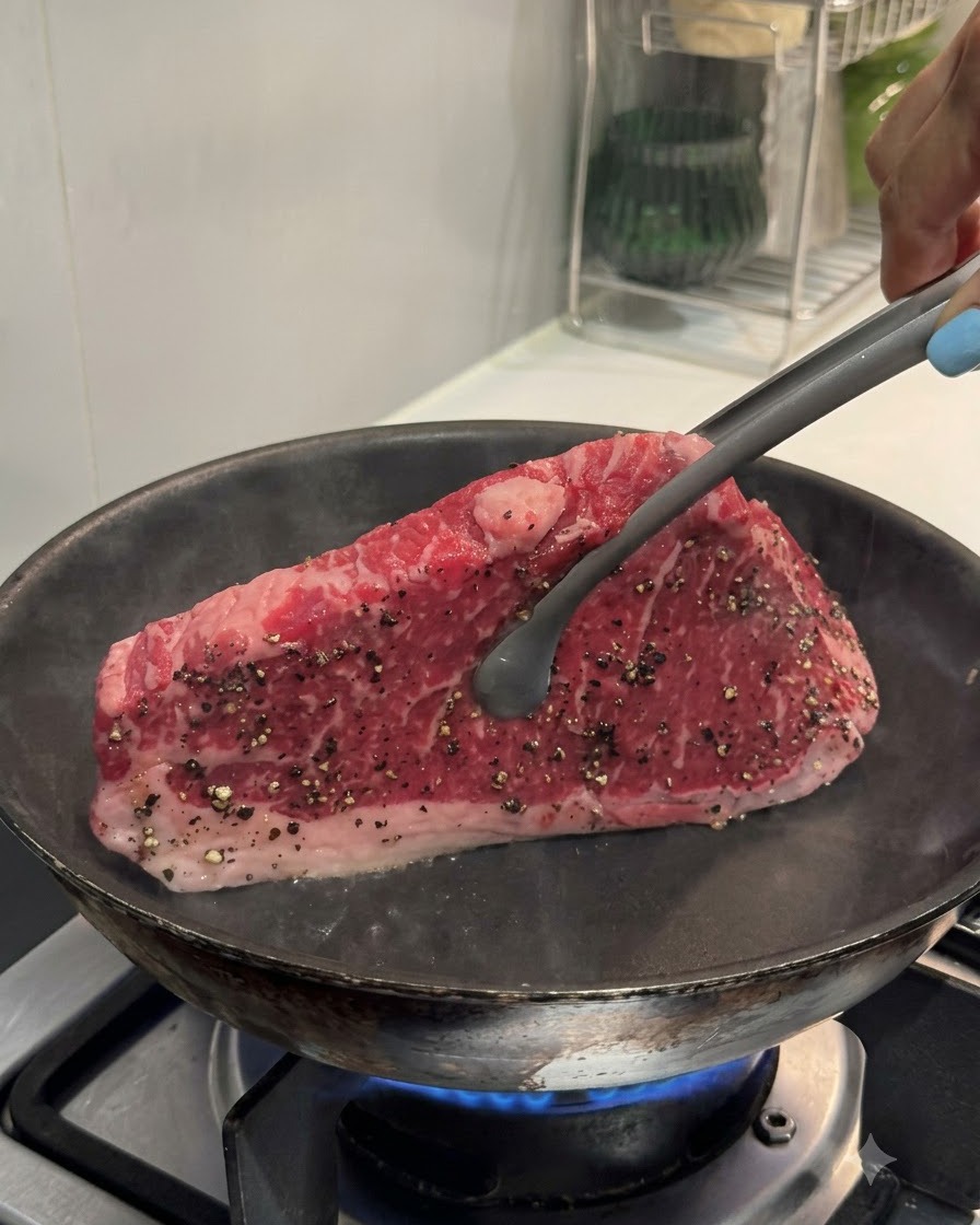Szczypce trzymające stek pionowo przy gorącej patelni w celu obsmażenia brzegu.