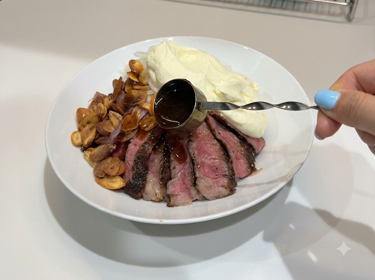 Ręka polewająca ciemnym, lśniącym sosem teriyaki gotową miseczkę ze stekiem i ryżem.