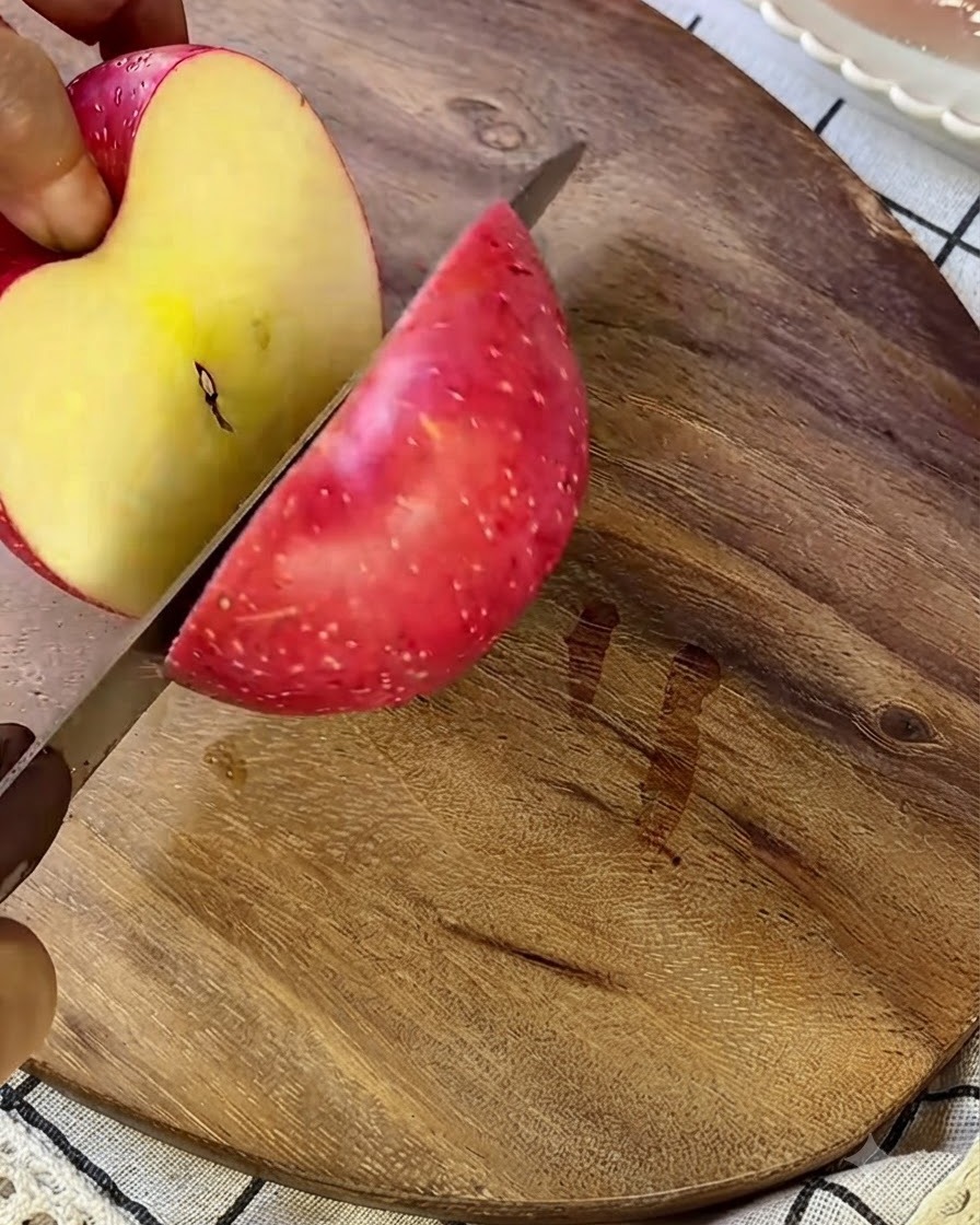 Jabłko krojone na małe kawałki na drewnianej desce do krojenia za pomocą srebrnego noża.