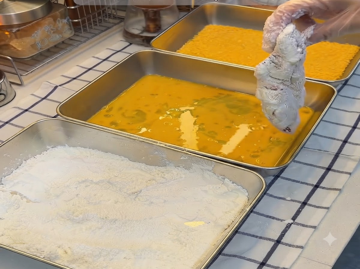 Kotlet wieprzowy obtoczony w skrobi zanurzani w naczyniu z roztrzepanymi żółtymi jajkami.