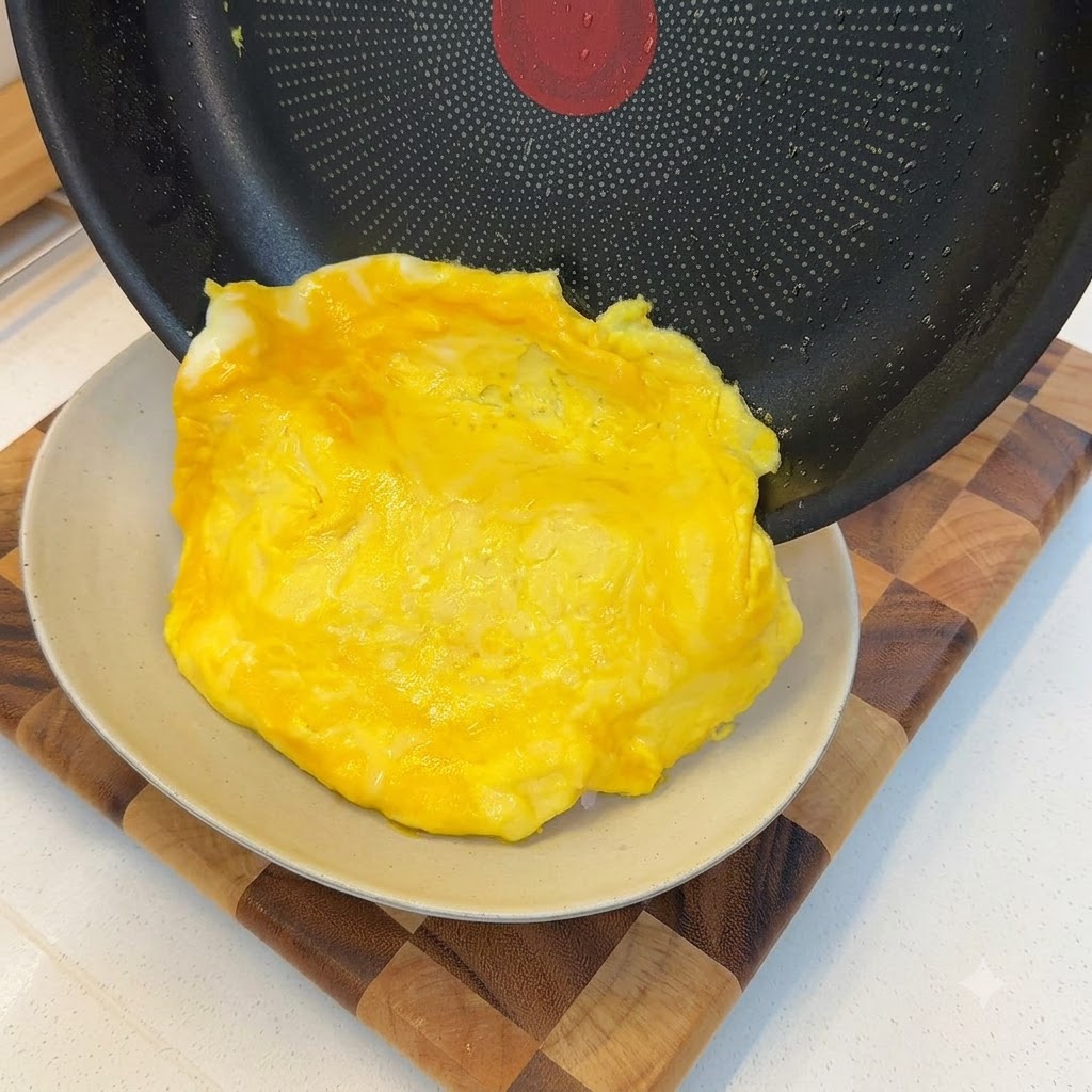 Miękki, usmażony omlet zsuwający się z patelni i nakładany na porcję białego ryżu.