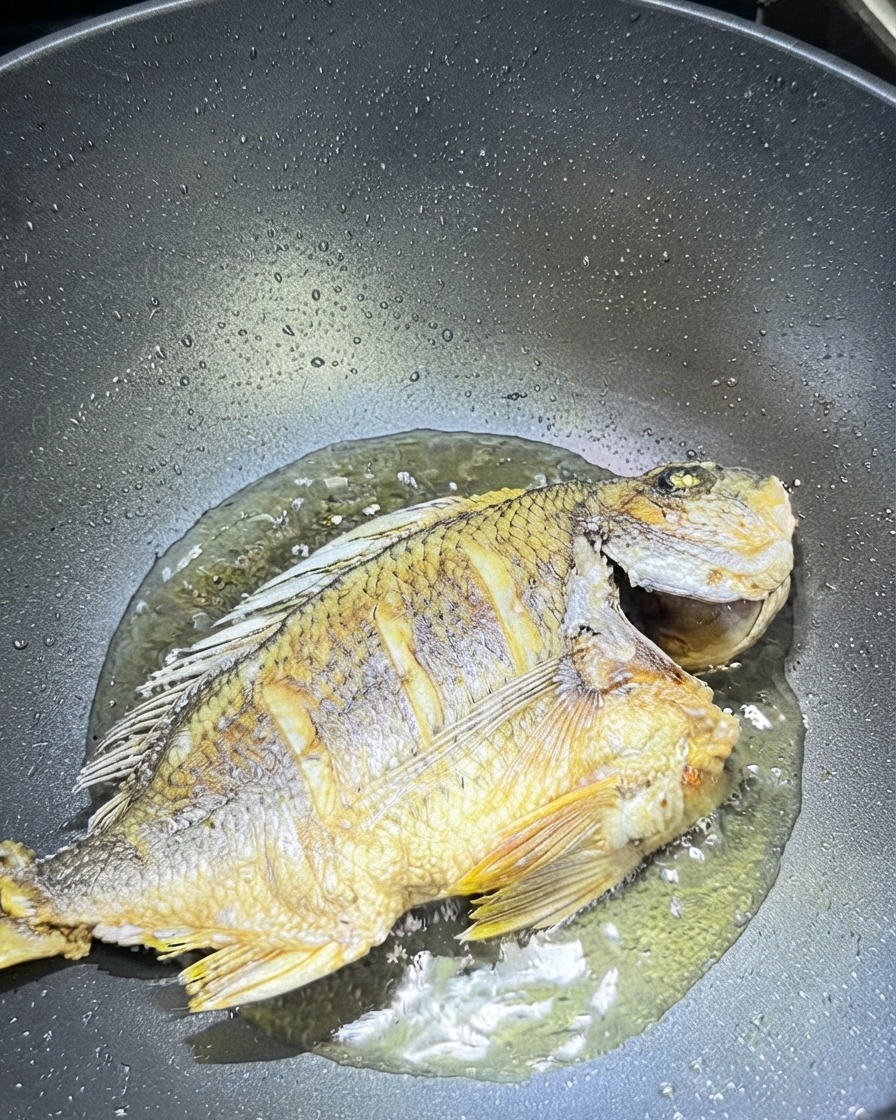 Pokrojony imbir i czosnek rozrzucone wokół smażonej ryby w woku.