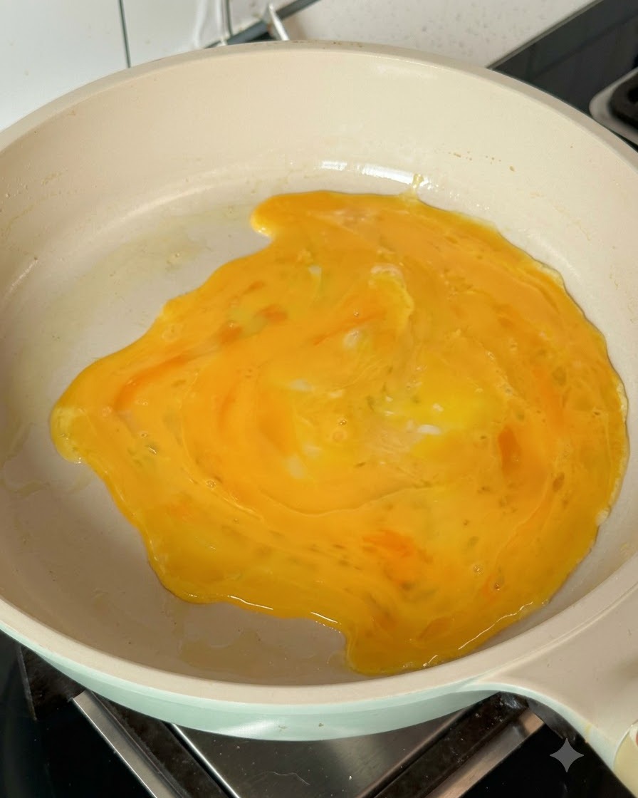 Roztrzepane jajka rozprzestrzeniające się po gorącej patelni, tworząc cienki omlet jajeczny.
