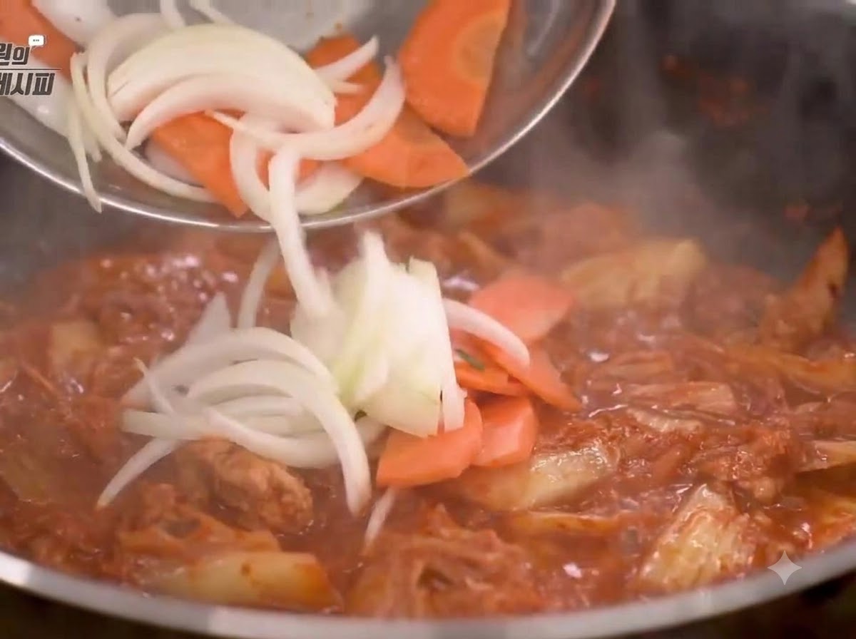 Pokrojona cebula i marchewka dodawane na patelnię i smażone z mieszanką kimchi.