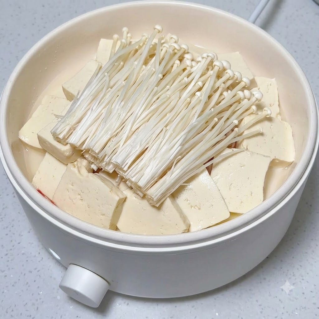 Plastry świeżego czerwonego chili ułożone schludnie na kopcu grzybów enoki i tofu w białym garnku.