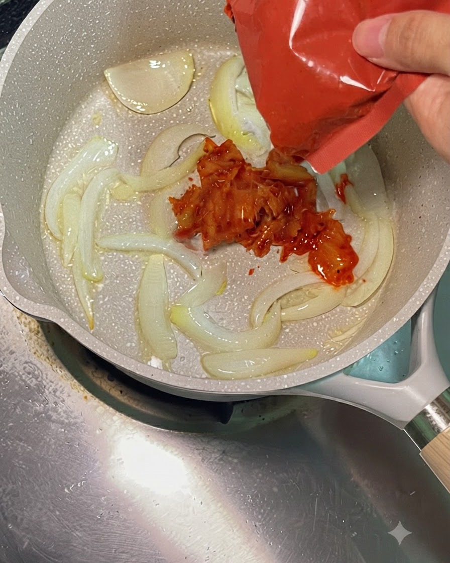 Jaskrawo czerwone posiekane kimchi dodawane z czerwonego opakowania do gorącej patelni z podsmażoną cebulą.