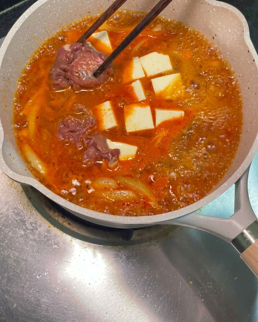 Pałeczki umieszczające surowe, marynowane plastry wołowiny w bulgoczącym garnku z czerwoną zupą.