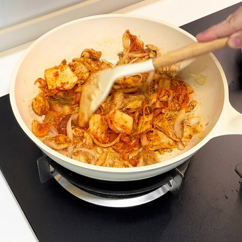 Kimchi i kurczak podsmażane razem na białej patelni za pomocą łopatki.