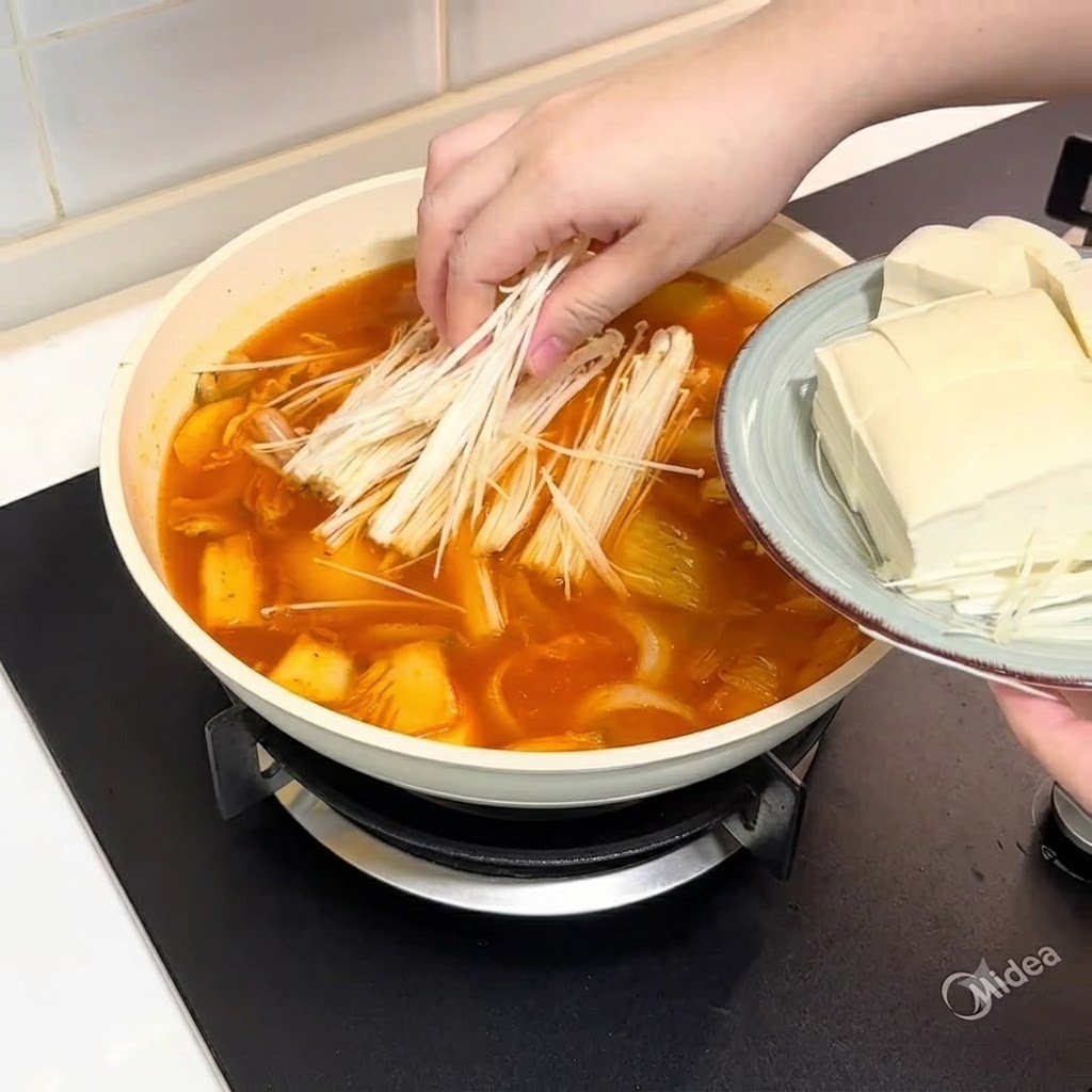 Grzyby enoki i pokrojone tofu dodawane do garnka z bulionem.