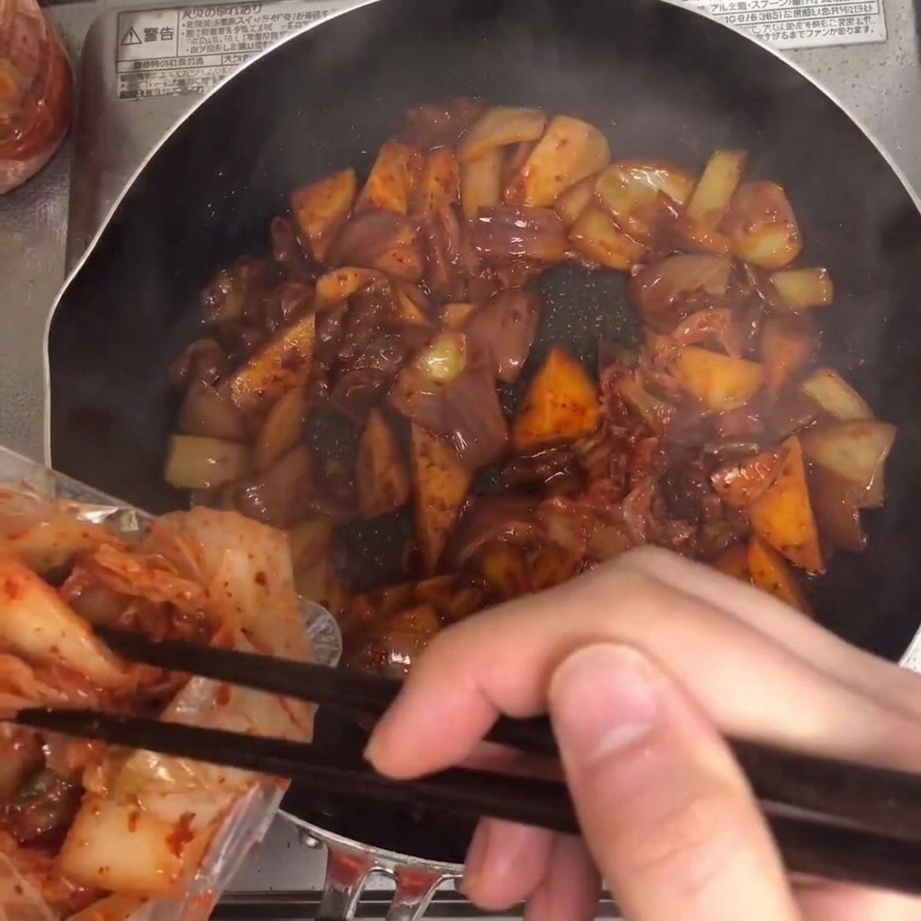 Kimchi dodawane do patelni i mieszane z pozostałymi składnikami.