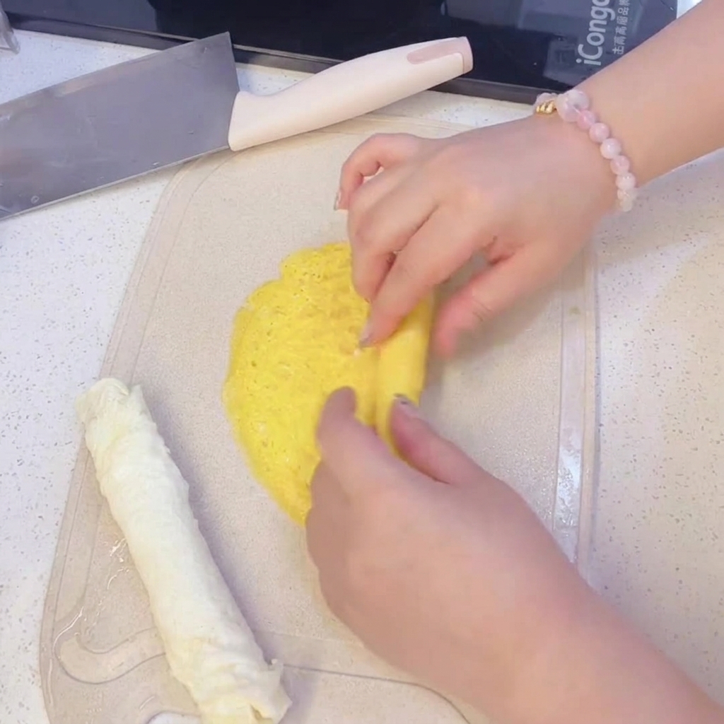 Ręce zwijające cienki żółty omlet jajeczny na desce do krojenia, obok zwiniętego wcześniej białego omletu.