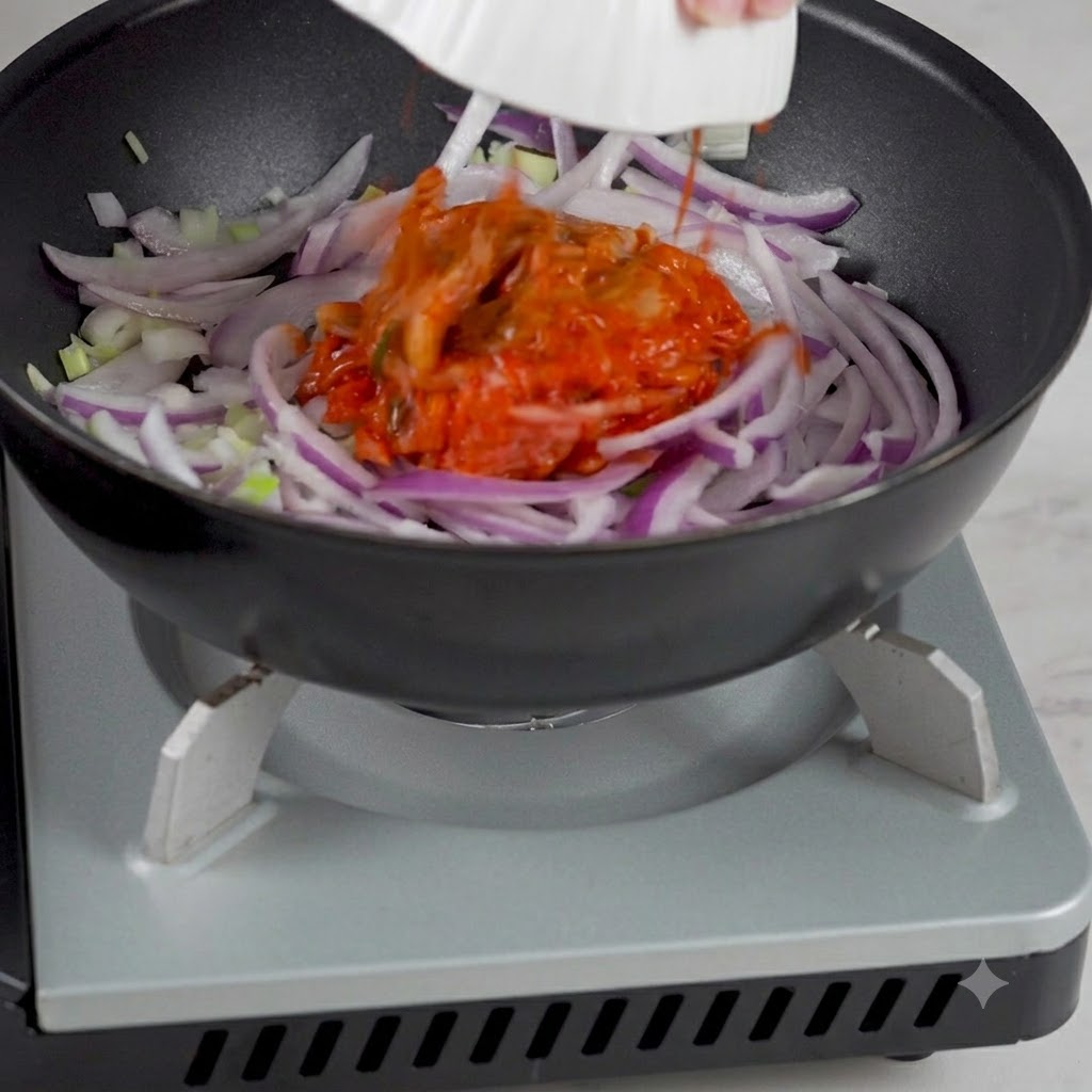 Koreańskie kimchi dodawane z miski do patelni zawierającej podsmażoną cebulę.