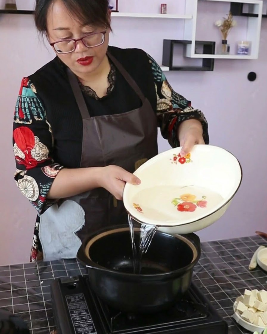 Czysta woda wlewana z ozdobnej miski do czarnego ceramicznego garnka stojącego na przenośnej kuchence.