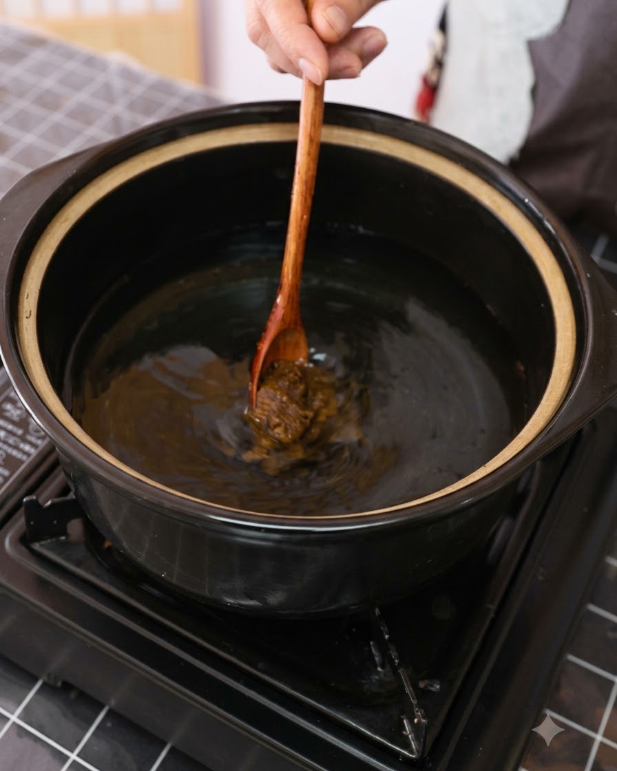Brązowa pasta sojowa mieszana w garnku z wodą za pomocą drewnianej łyżki.