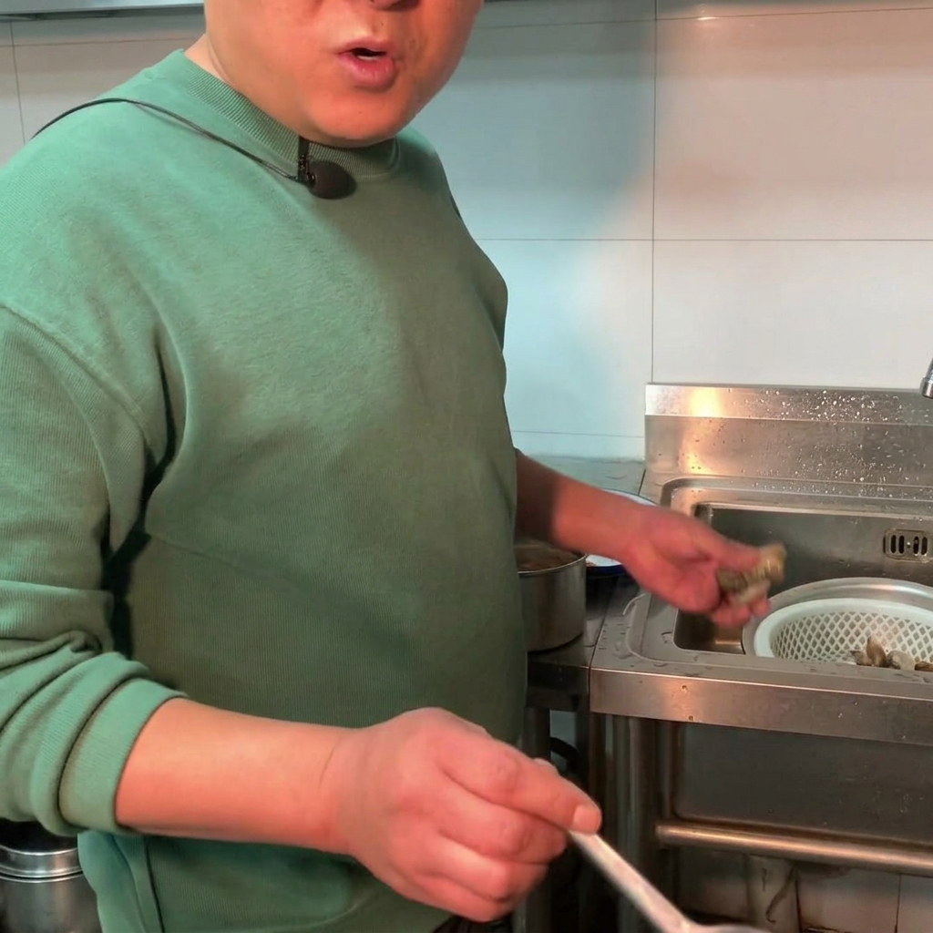 Świeże małże wrzucane do garnka z gotującym się gulaszem z pasty sojowej.
