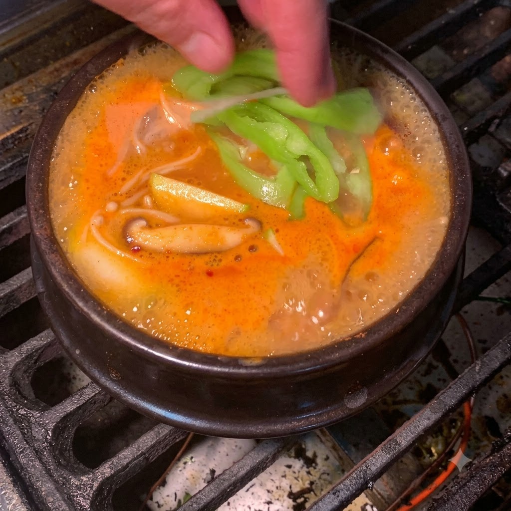 Plasterki świeżego zielonego chili wrzucane do bulgoczącego pomarańczowo-czerwonego koreańskiego gulaszu z pasty sojowej.