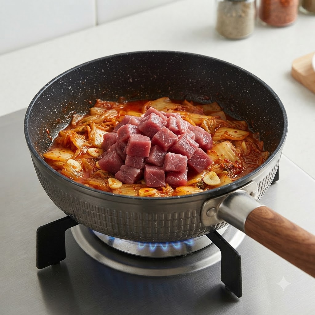 Surowe kostki wołowe ułożone na wierzchu podsmażonego kimchi w garnku.