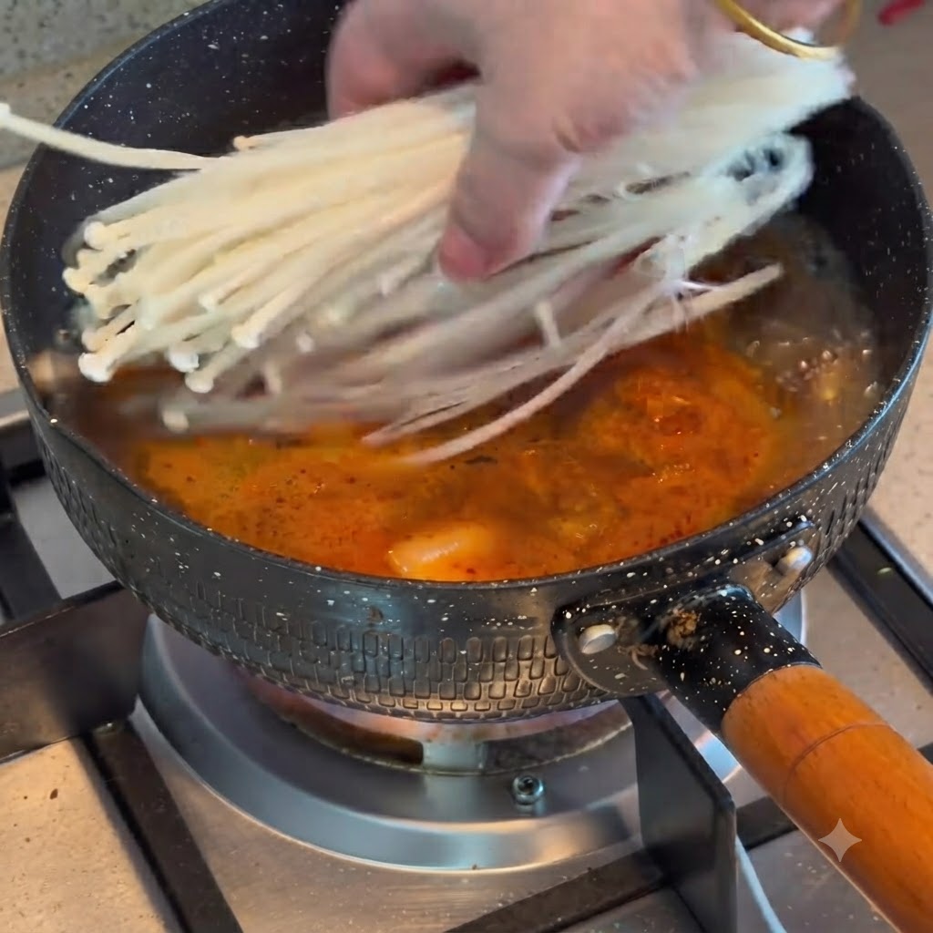 Grzyby enoki dodawane do garnka z wrzącym gulaszem z kimchi i wołowiny.