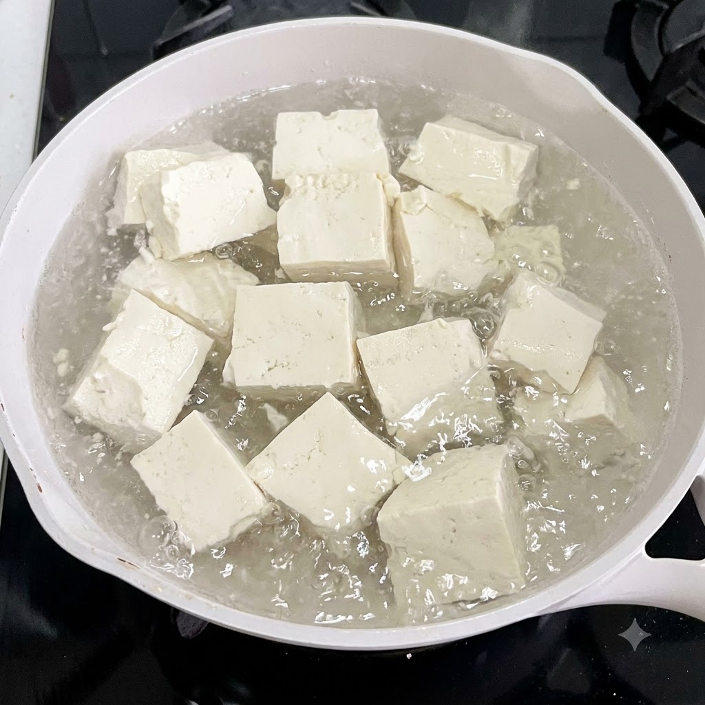 Kostki tofu gotujące się w białym garnku z wodą i plastrami imbiru.