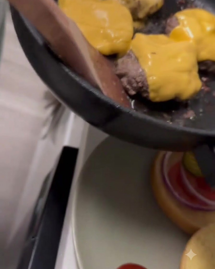 Żółty ser cheddar topiący się na wierzchu kotletów wołowych na patelni.
