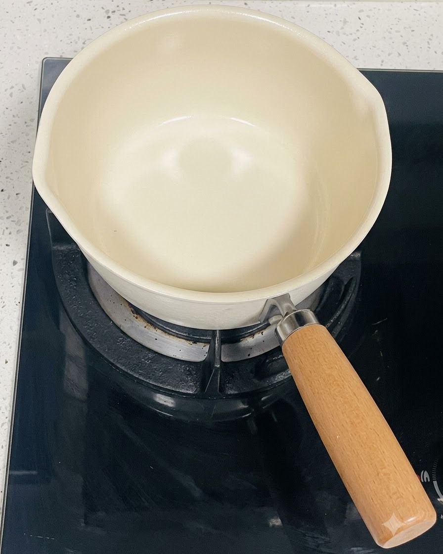 Pusty garnek w kolorze kremowym stojący na czarnym palniku płyty indukcyjnej.