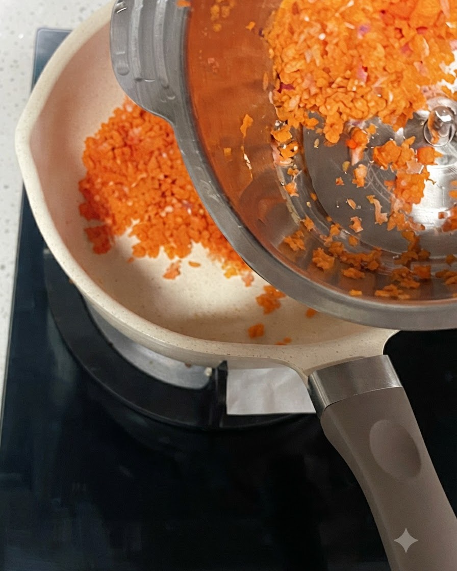 Posiekana marchewka i cebula wsypywane ze stalowego pojemnika do rozgrzanego garnka.