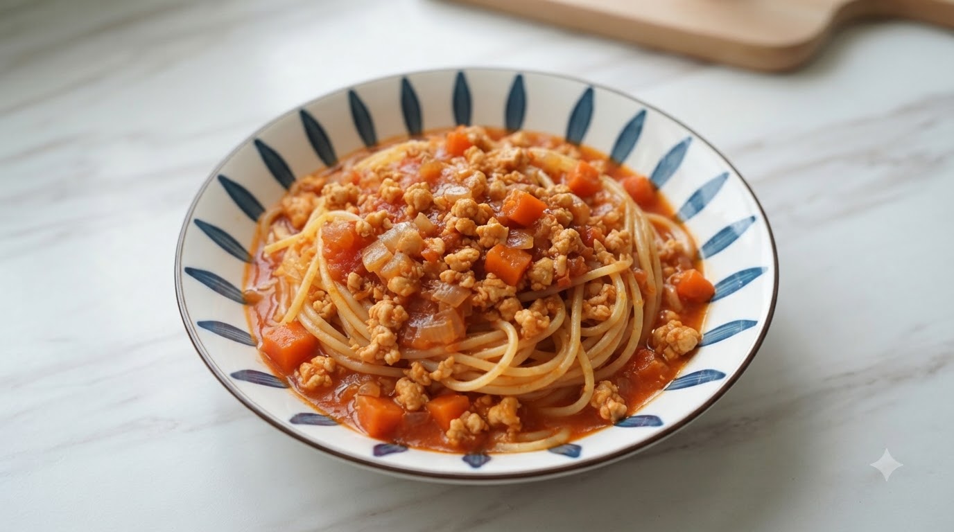 Talerz spaghetti polany gęstym sosem z kurczaka i pomidorów, udekorowany kawałkami marchewki i cebuli