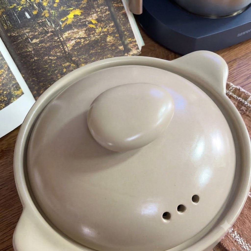 Świeże pomidory ułożone na kratce obok ceramicznego garnka.