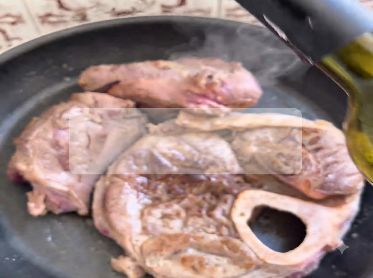 Czerwone wino nalewane z butelki na obsmażoną wołowinę skwierczącą na gorącej patelni.