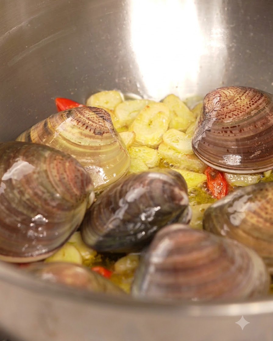 Białe wino wlewane z butelki na patelnię wypełnioną małżami, czosnkiem i chili.