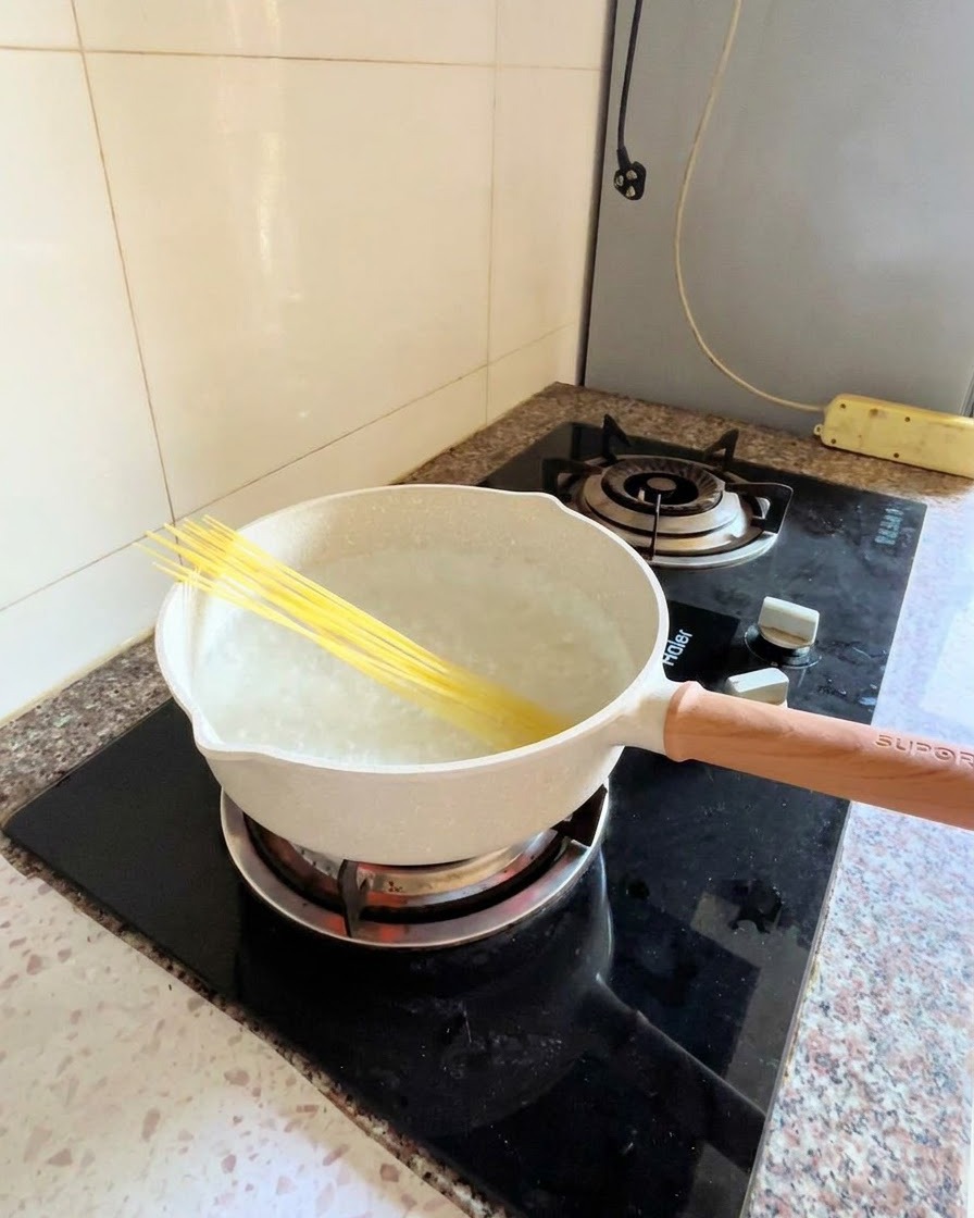 Surowe nitki spaghetti umieszczone ukośnie w garnku z gotującą się wodą na kuchence.