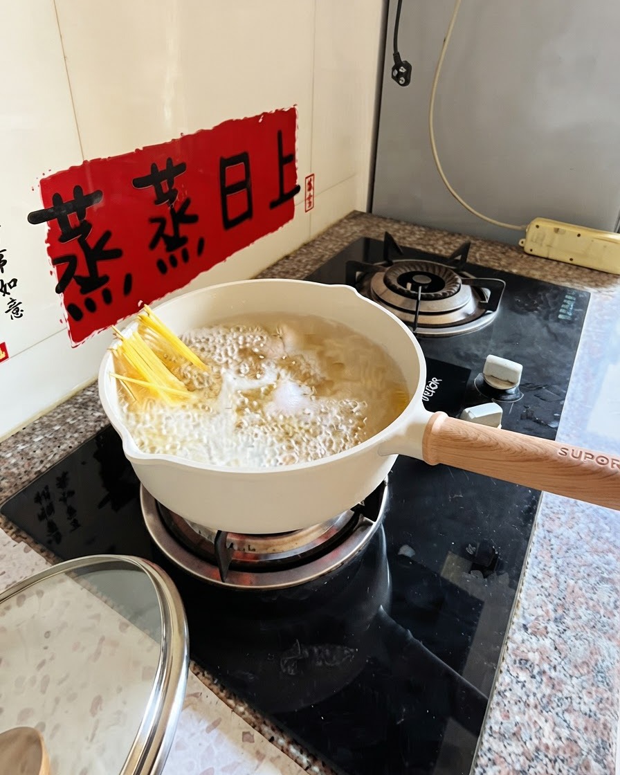 Spaghetti gotujące się w białym garnku z szczypcami częściowo zanurzającymi nitki.