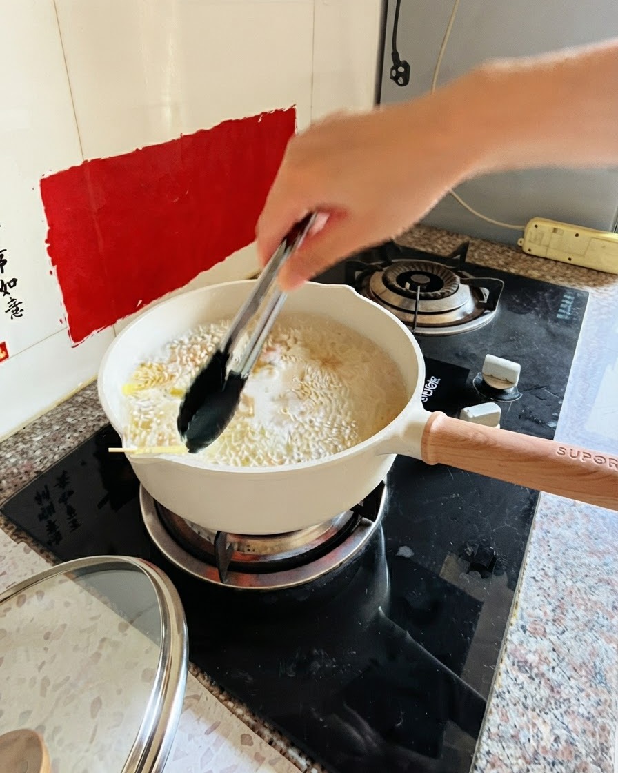Szczypce mieszające makaron w garnku z gotującą się wodą na kuchence.