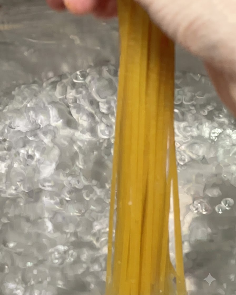 Makaron spaghetti wkładany do dużego garnka z gotującą się, bąbelkującą wodą.